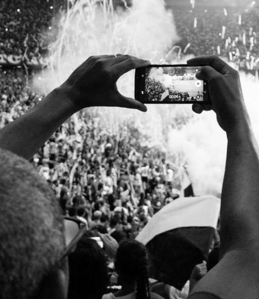 Photo of a man taking a picture on his phone at a sports event